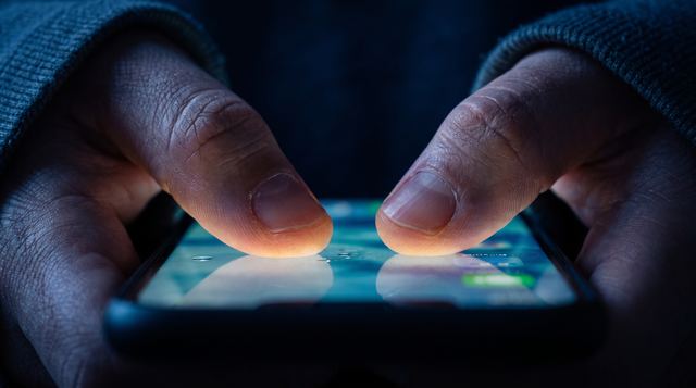 Nahaufnahme zweier Daumen, die im Dunkeln auf einem leuchtenden Smartphone tippen.